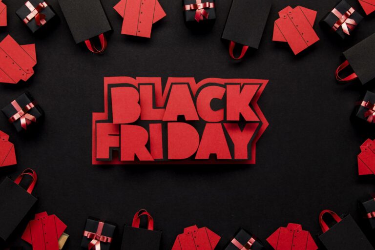 Lettres BLACK FRIDAY découpées dans du papier rouge sur fond noir, entourées de sacs de courses, de chemises et de paquets cadeaux en papier