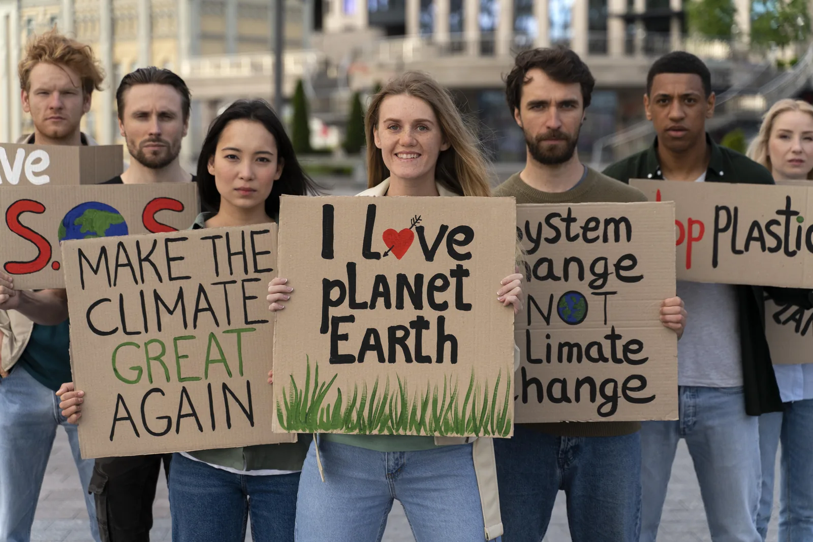 Groupe de jeunes manifestants dans une rue, tenant des pancartes en carton pour le climat, dont « I love planet Earth » et « Make the climate great again »