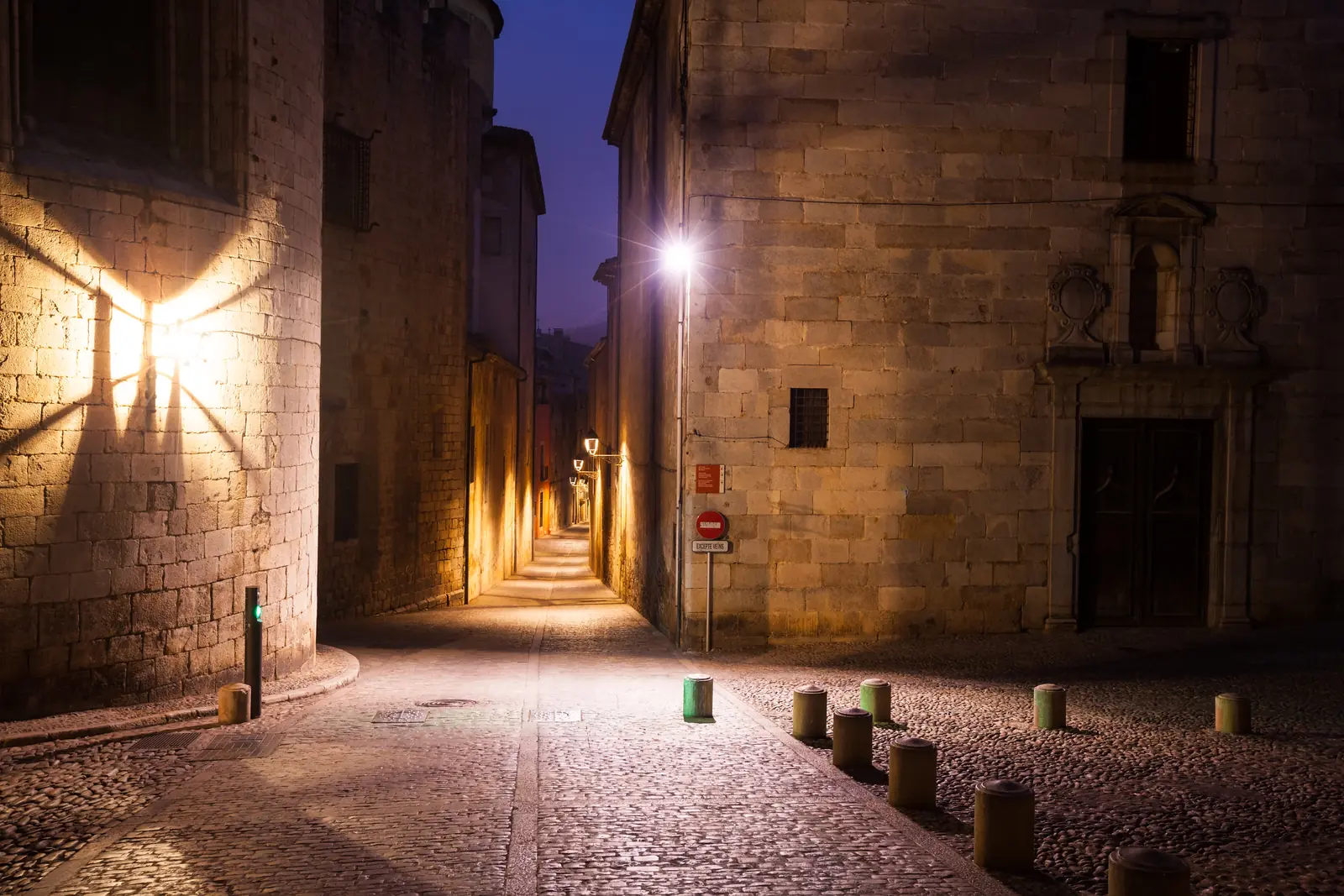 Ruelle pavée d'une vieille ville, déserte la nuit, éclairée par des lanternes sur des murs de pierre
