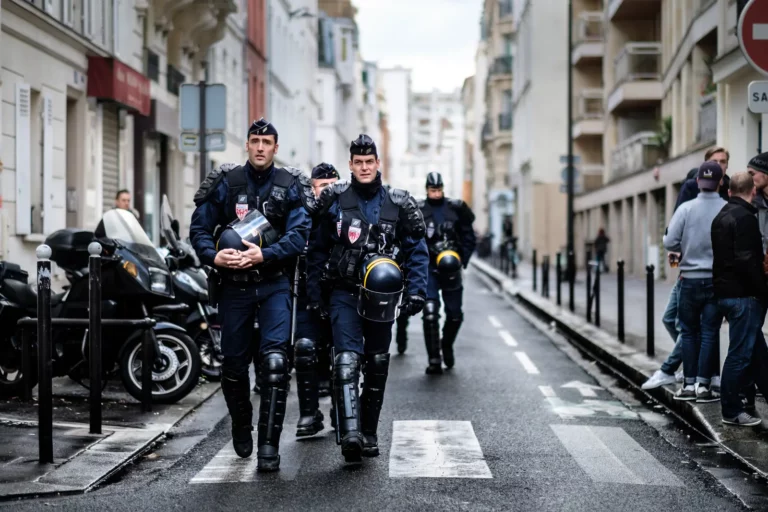 Policiers français en tenue de maintien de l'ordre, casque à la main, marchant au milieu d'une rue de Paris