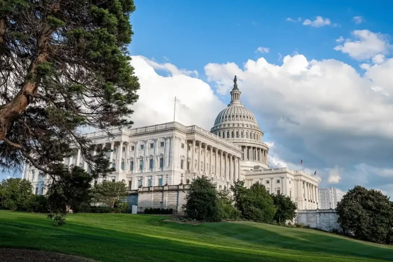 Le Capitole des États-Unis à Washington, avec son dôme blanc, vu depuis une pelouse en pente sous un ciel bleu chargé de nuages