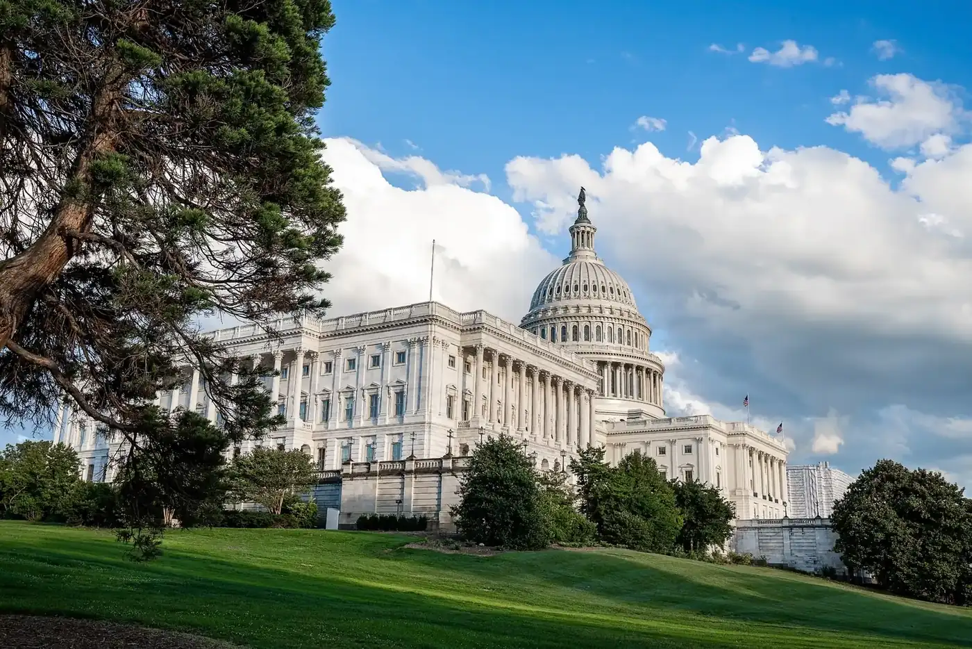 Le Capitole des États-Unis à Washington, avec son dôme blanc, vu depuis une pelouse en pente sous un ciel bleu chargé de nuages